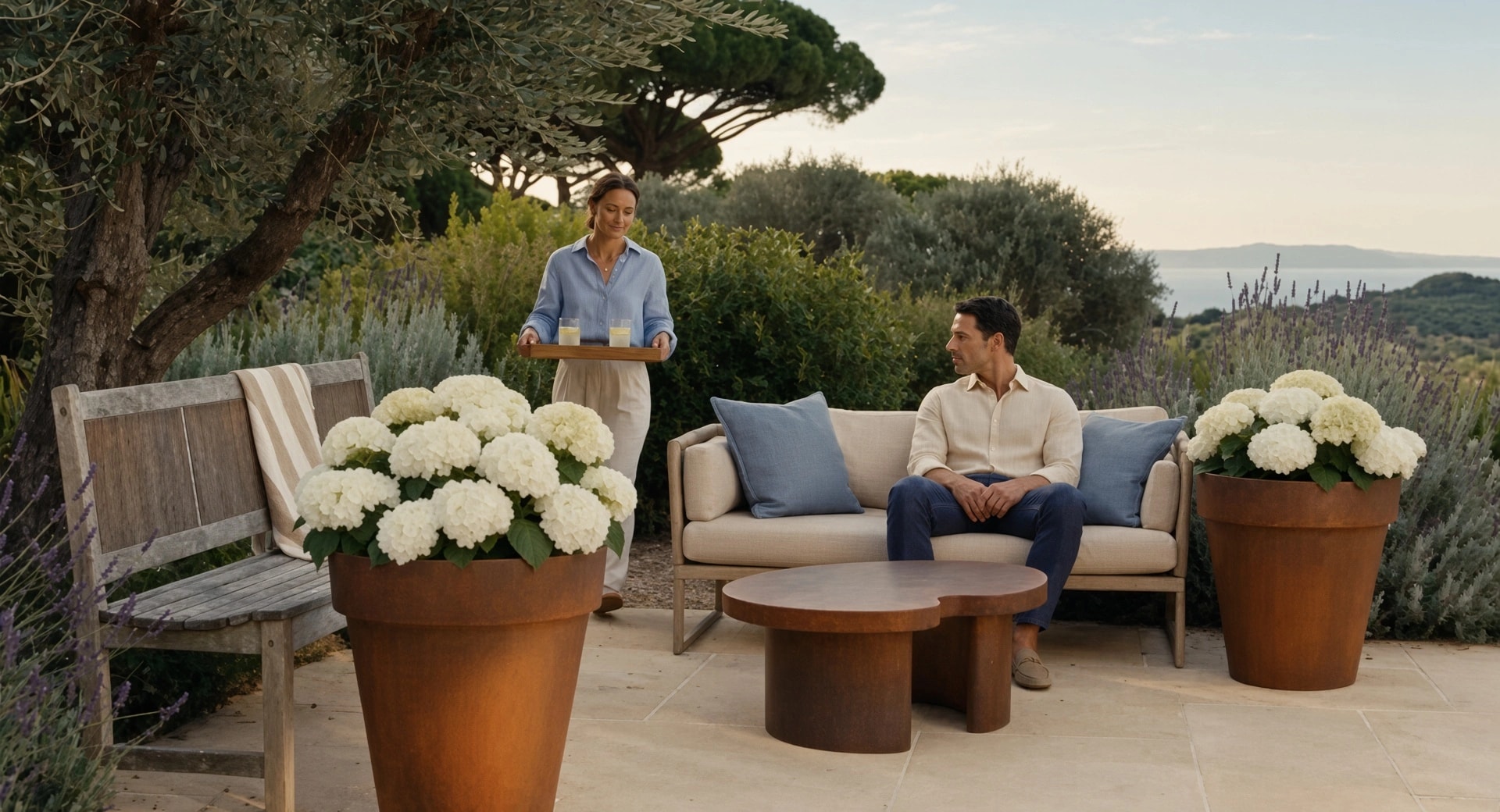 Deux pots de fleurs coniques Calypso en acier Corten aux hortensias blancs, sur une terrasse avec vue sur la mer