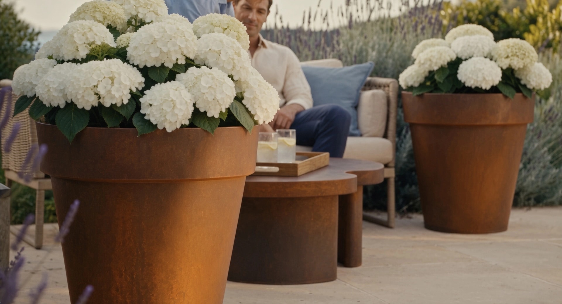Pot de fleurs conique Calypso en acier Corten aux hortensias blancs au premier plan d'un salon de jardin