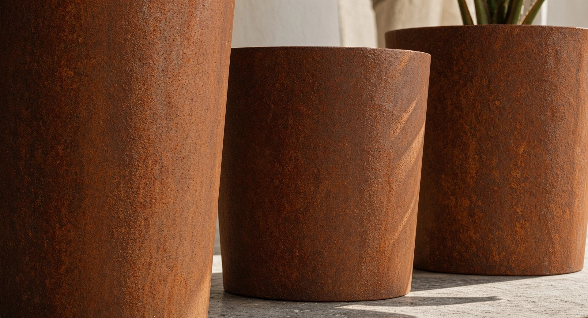 Gros plan sur trois pots de fleurs ronds élancés Clio en acier Corten, patine rouille au premier plan