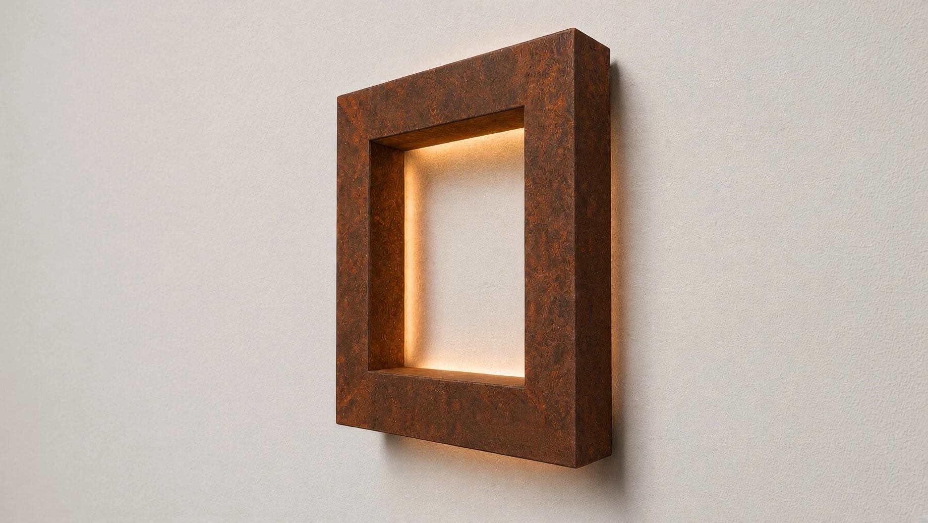 Applique carrée Aura en acier Corten allumée, vue de trois quarts sur un mur clair