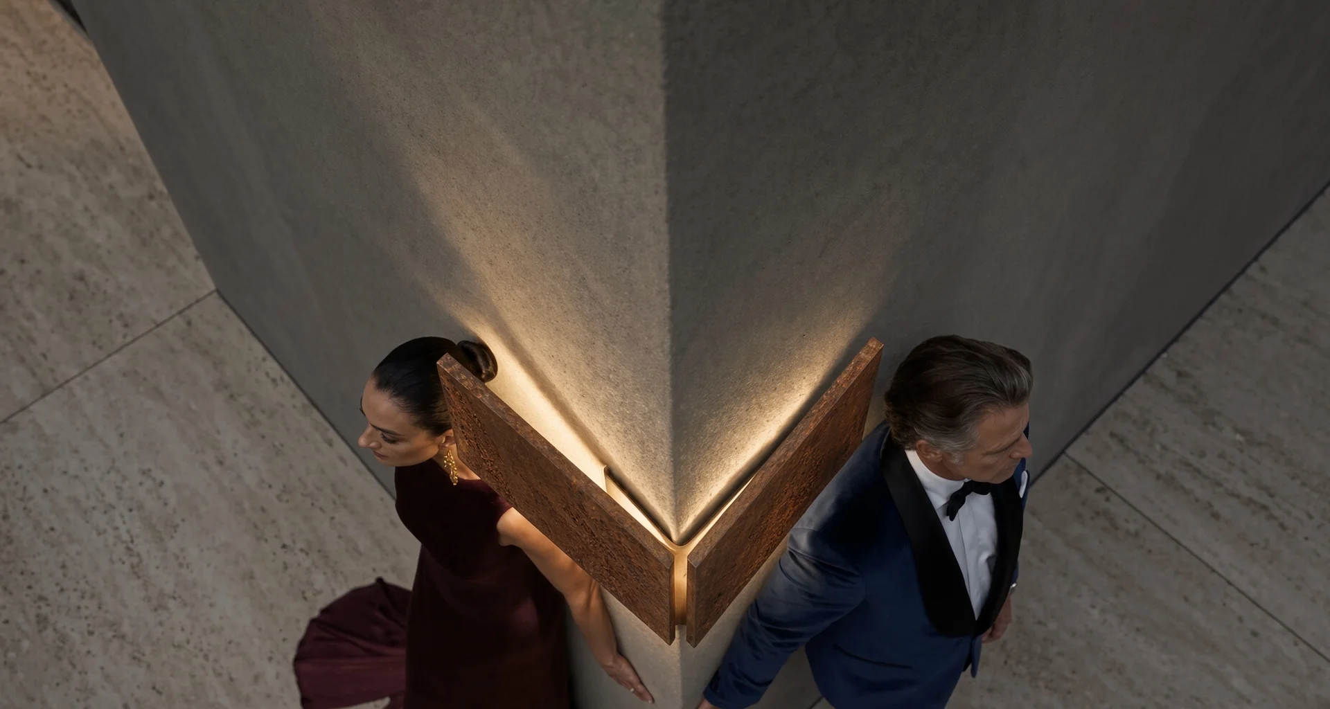 Applique Angle Dièdre en acier Corten en vue plongeante, un couple en tenue de soirée au pied du mur