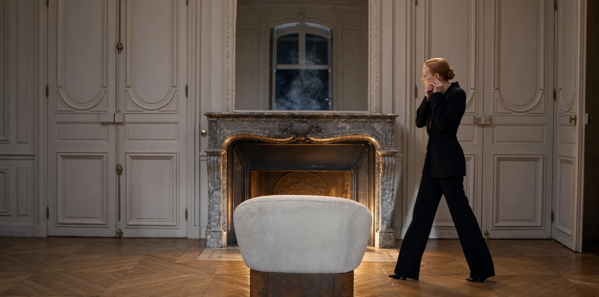 Fauteuil Hestia en acier Corten vu de dos devant une cheminée allumée, une femme debout dans un salon à boiseries