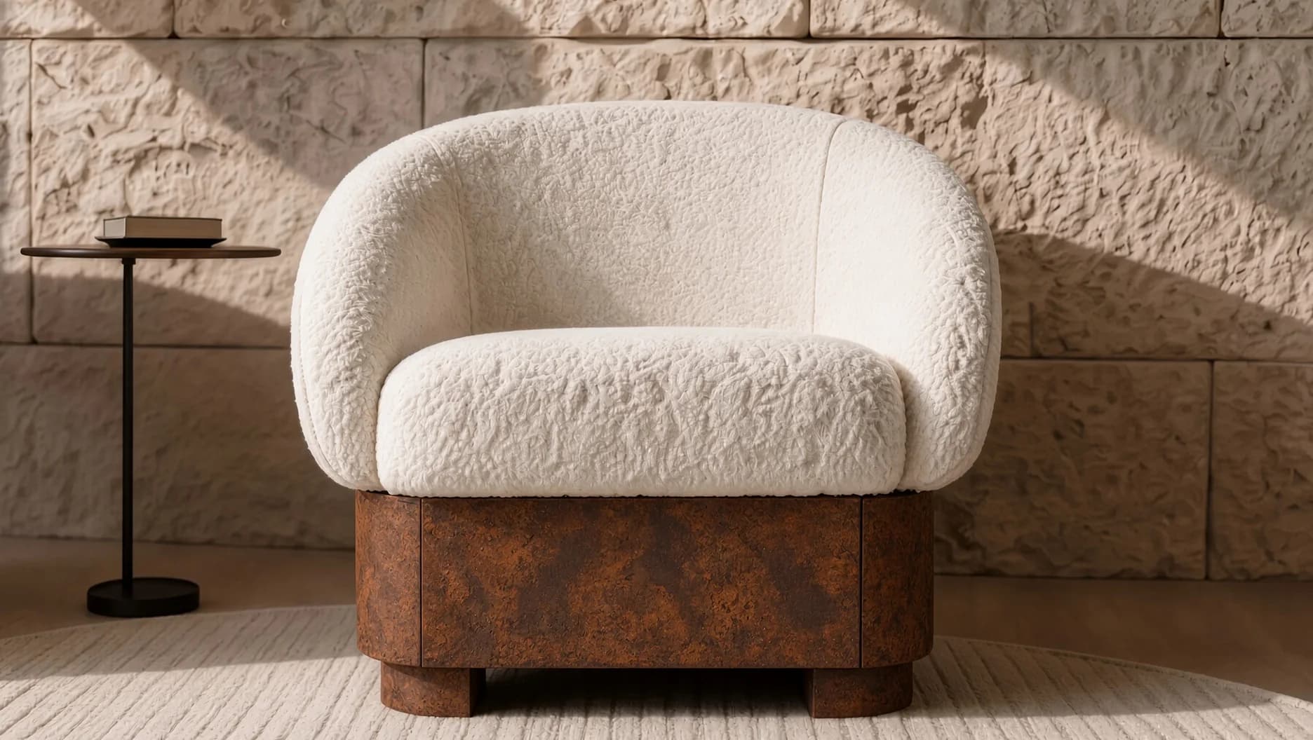 Fauteuil Hestia en bouclé écru sur socle en acier Corten devant un mur de pierre éclairé par le soleil