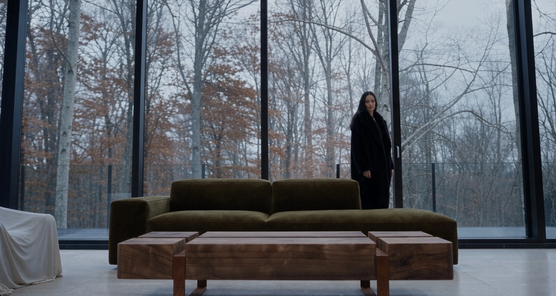 Table basse Silas en acier Corten devant un canapé vert, dans un pavillon vitré ouvert sur une forêt, une femme debout
