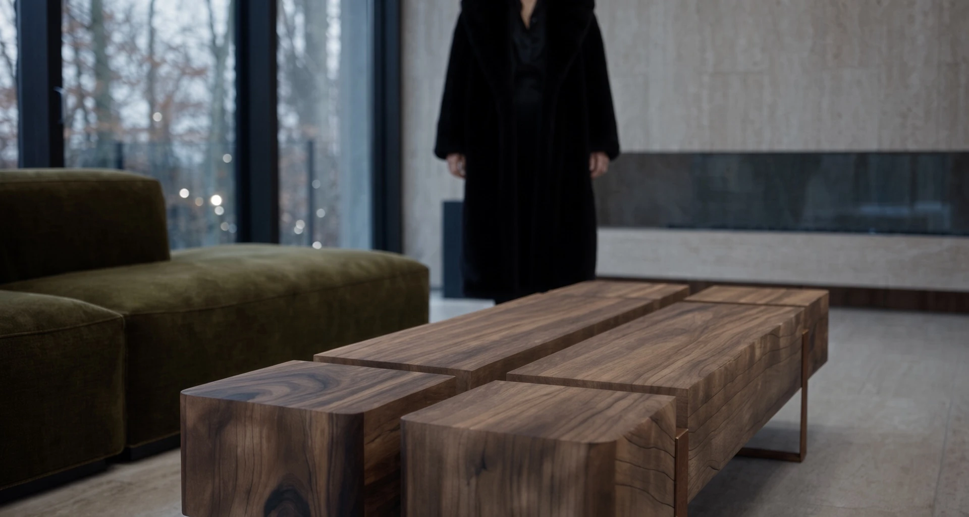 Table basse Silas en acier Corten au premier plan, canapé en velours vert et silhouette en manteau noir