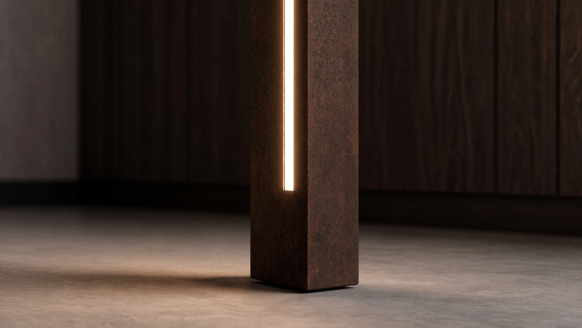 Gros plan du pied du lampadaire Sirius en acier Corten, sa fente lumineuse éclairant un sol en béton