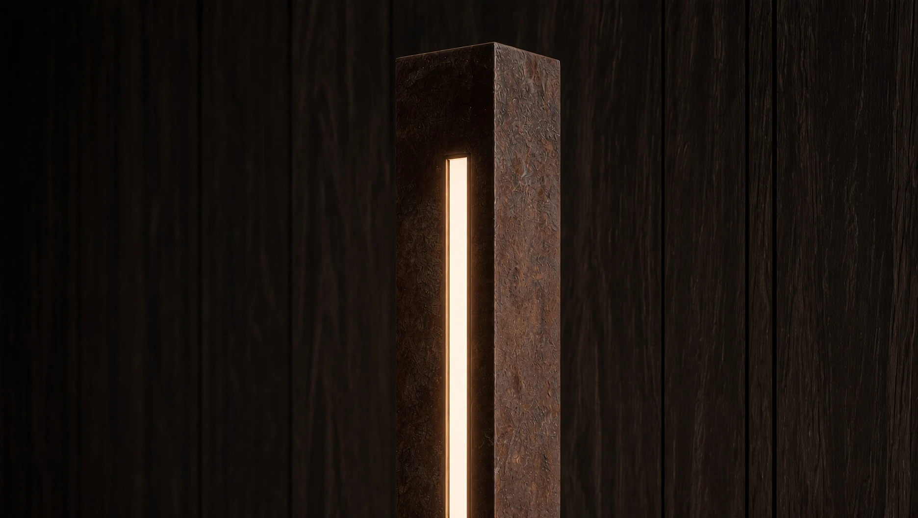 Détail du haut du lampadaire Sirius en acier Corten et de sa fente lumineuse, devant des panneaux de bois sombre