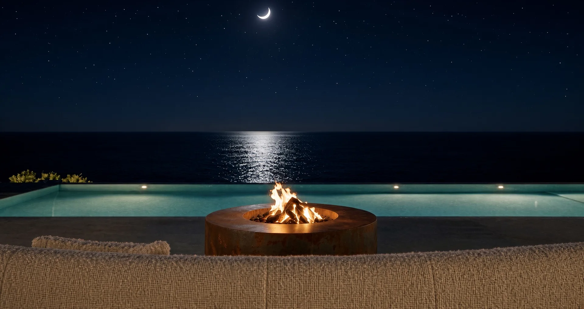 Table de feu Hélios en acier Corten allumée de nuit au bord d'une piscine à débordement, sous un croissant de lune