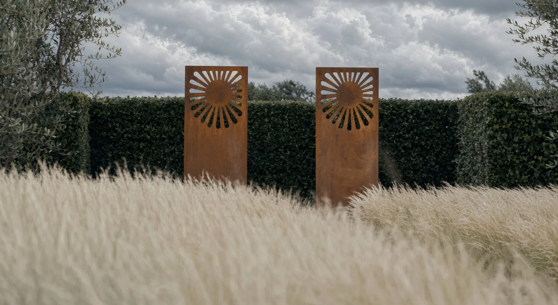 Deux panneaux décoratifs Éole en acier Corten à motif de soleil dans un jardin de haies, graminées au premier plan