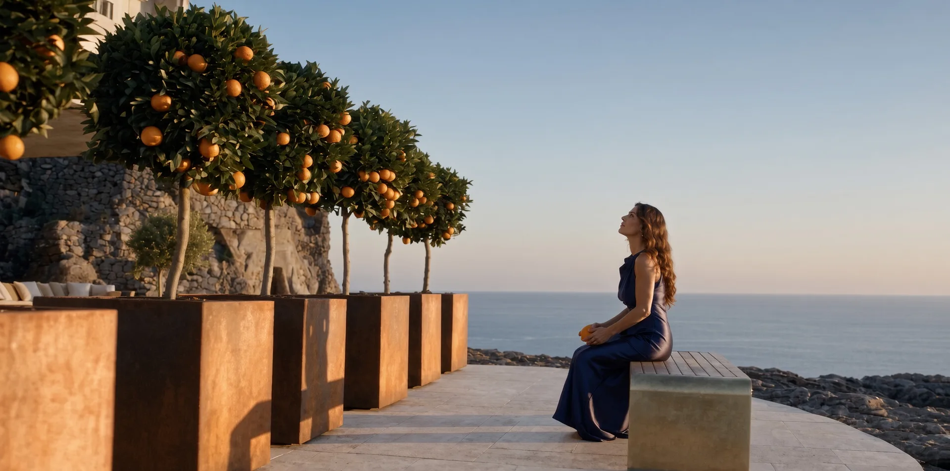 Alignement de jardinières carrées Cybèle en acier Corten avec orangers sur une terrasse en bord de mer, une femme assise