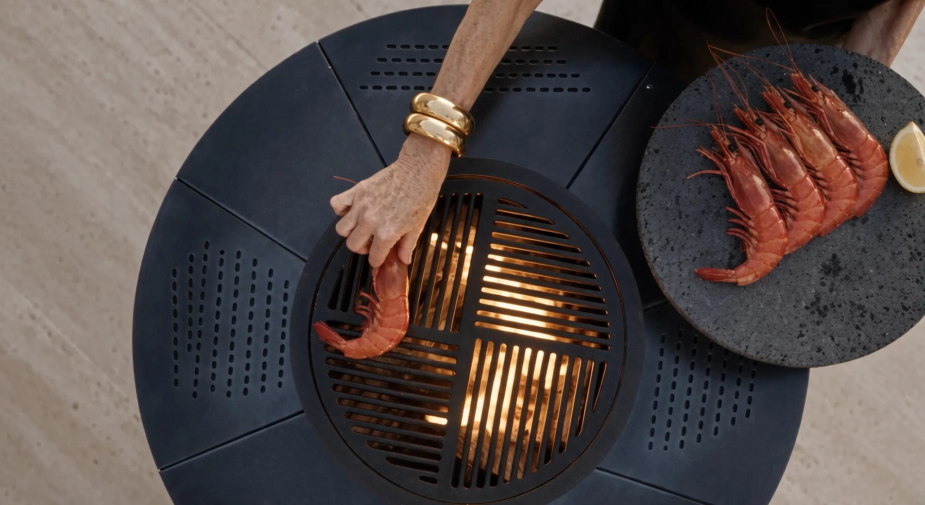 Vue de dessus du barbecue Vulcain en acier Corten, une main posant des gambas sur la grille