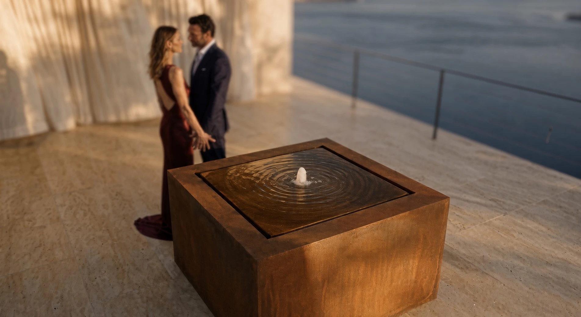 Fontaine carrée Alban en acier Corten sur une terrasse face à la mer, un couple en tenue de soirée derrière
