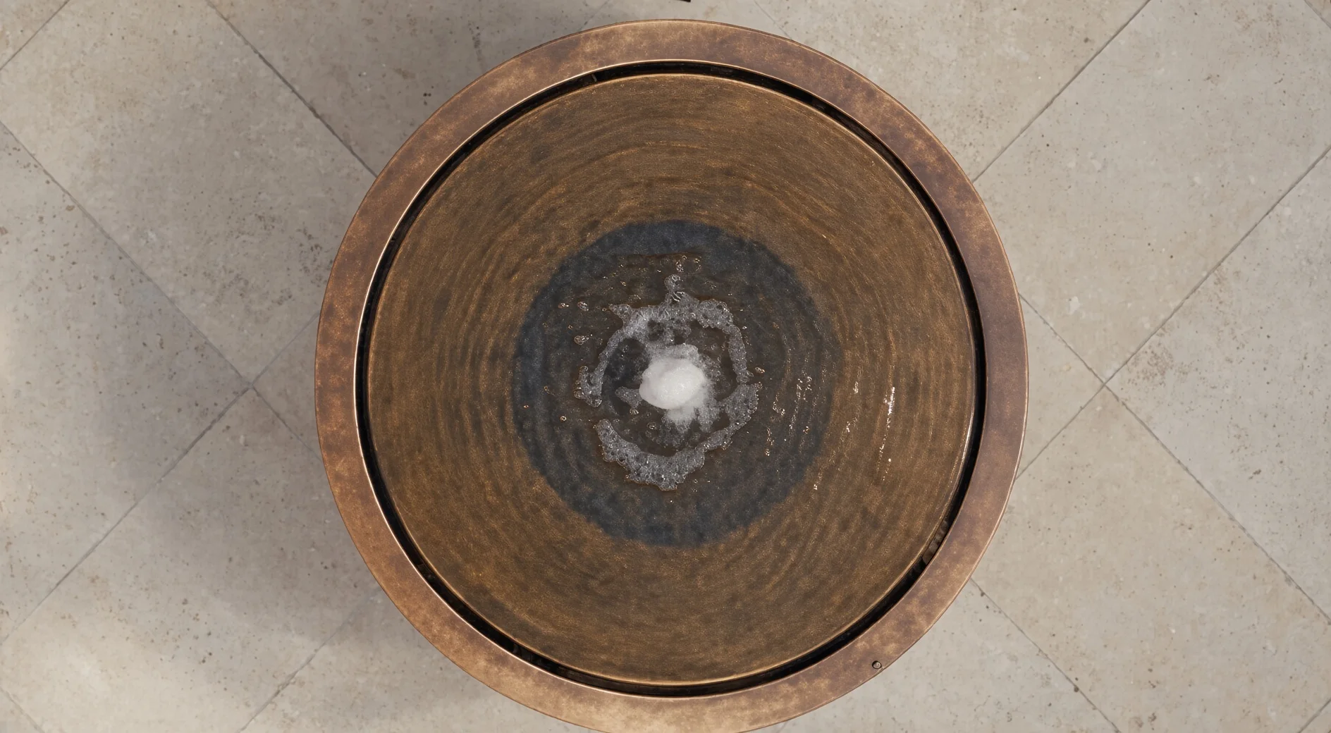 Fontaine ronde Elio en acier Corten vue de dessus sur un dallage clair, jet au centre du miroir d'eau