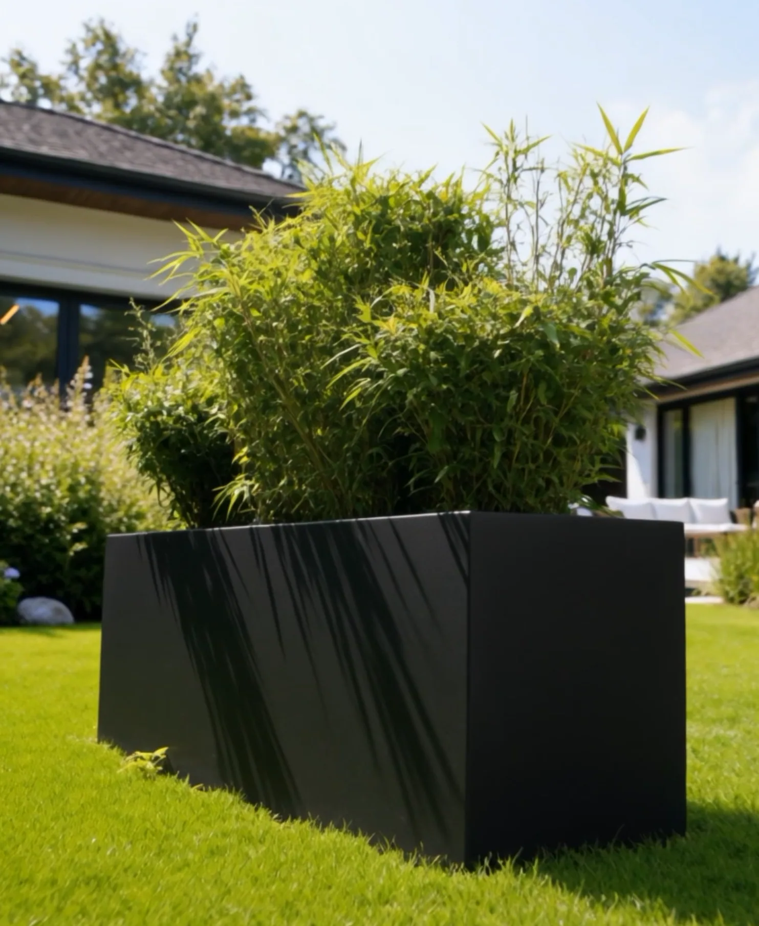 Jardinière rectangulaire Déméter en aluminium noir en contre-plongée, reflets sur les parois, maison derrière