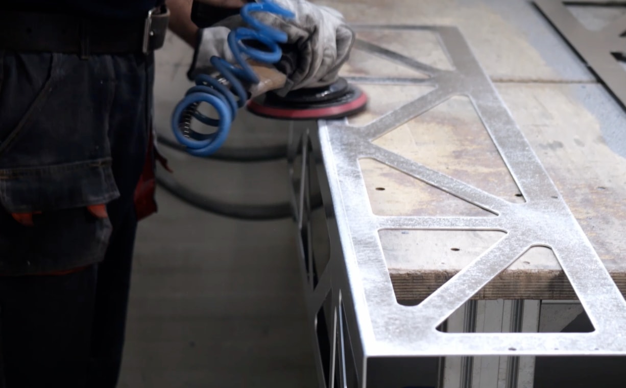 Ponçage d'une pièce métallique ajourée à la ponceuse pneumatique dans l'atelier Cortenys