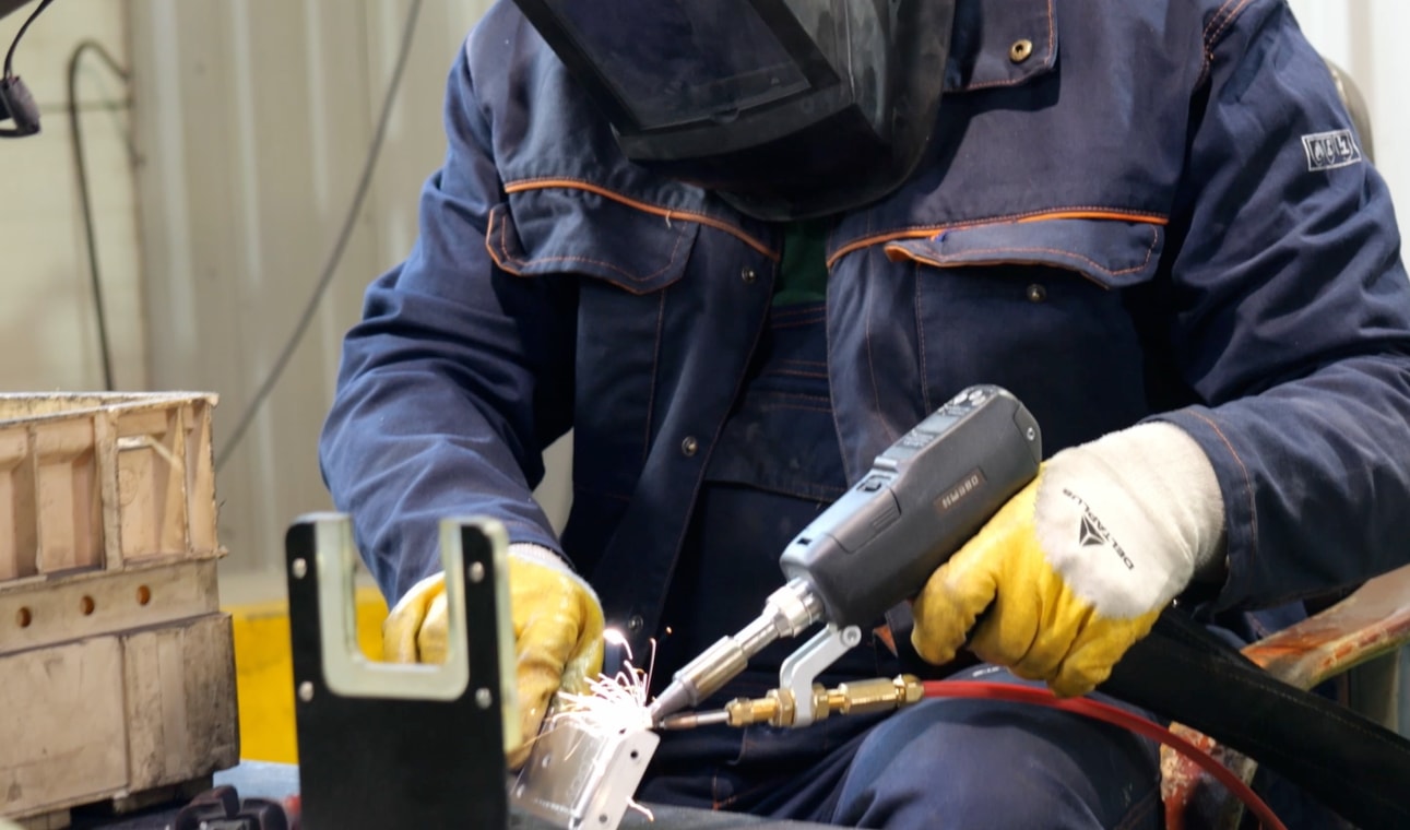 Soudeur casqué et ganté assemblant une petite pièce métallique à la torche dans l'atelier Cortenys