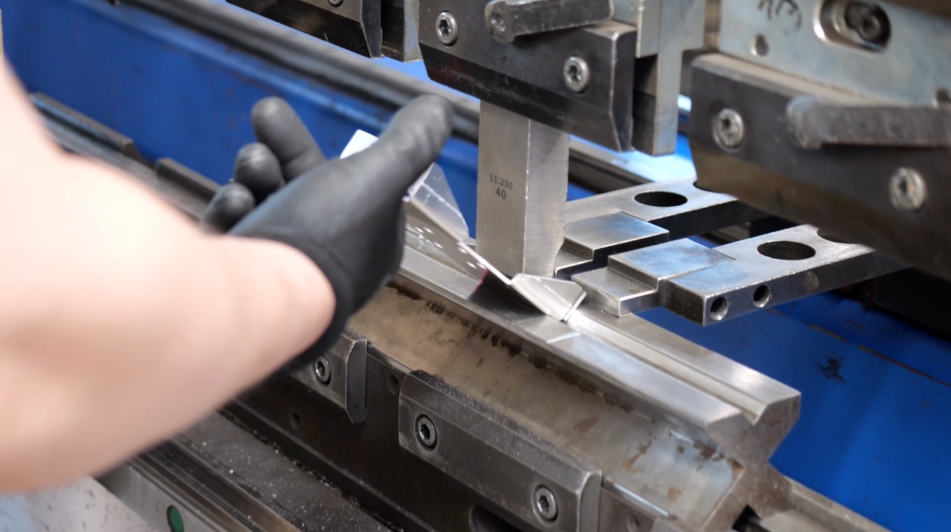 Bending a sheet-metal part on a press brake in the Cortenys workshop, close-up of a gloved hand