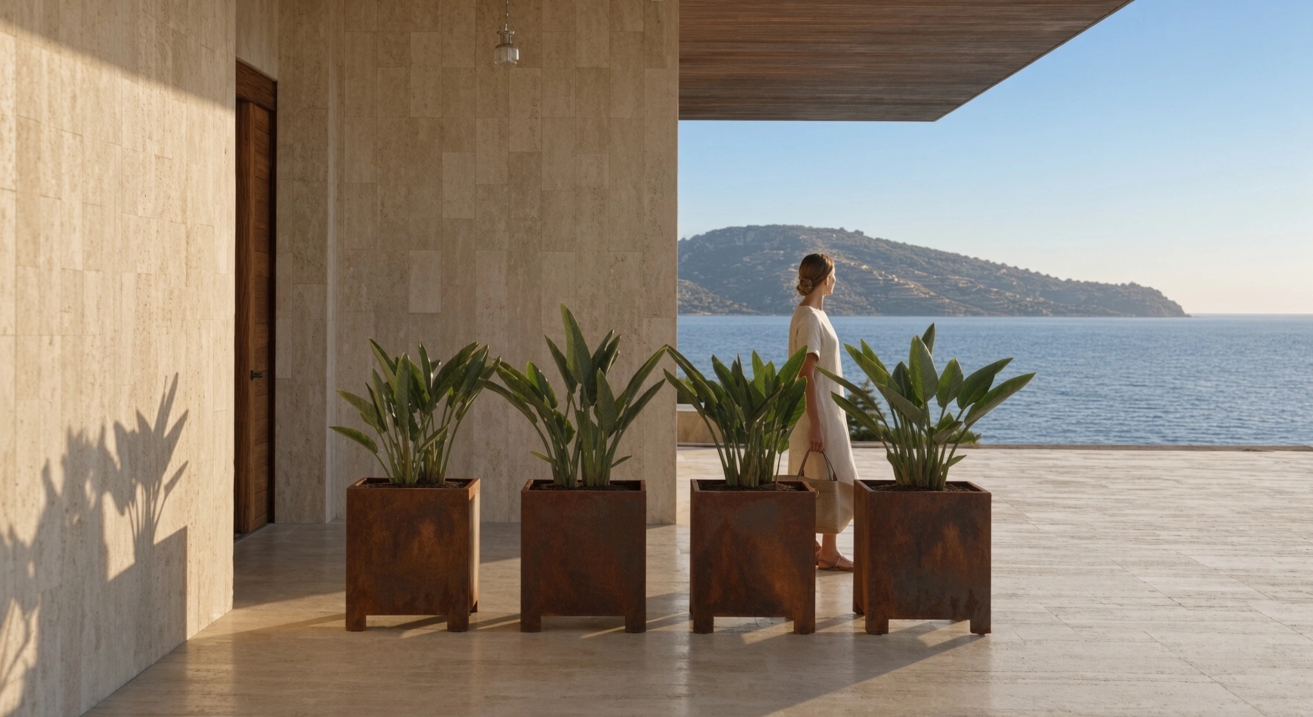 Jardinières carrées Thalie en acier Corten sur pieds sous une loggia face à la mer, une femme marchant entre elles
