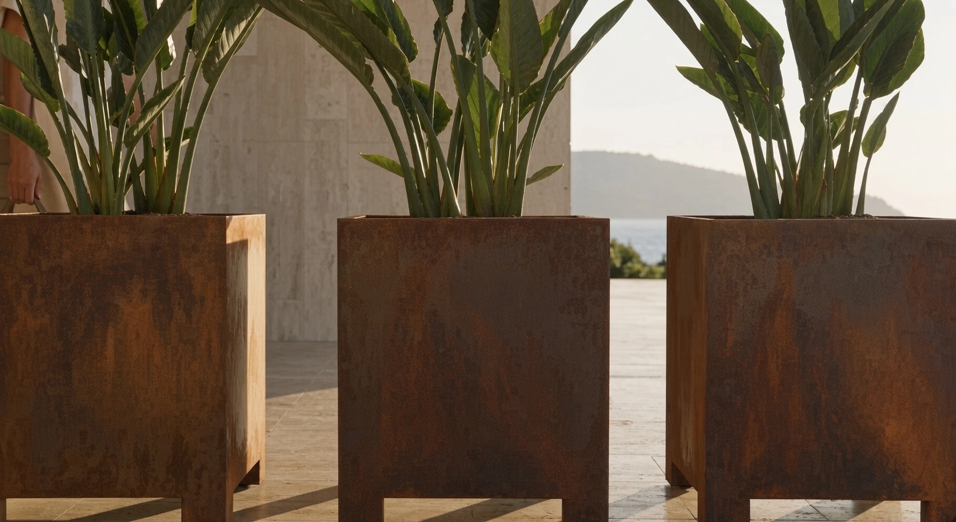 Trois jardinières carrées Thalie en acier Corten sur pieds en plan serré, la mer visible entre elles