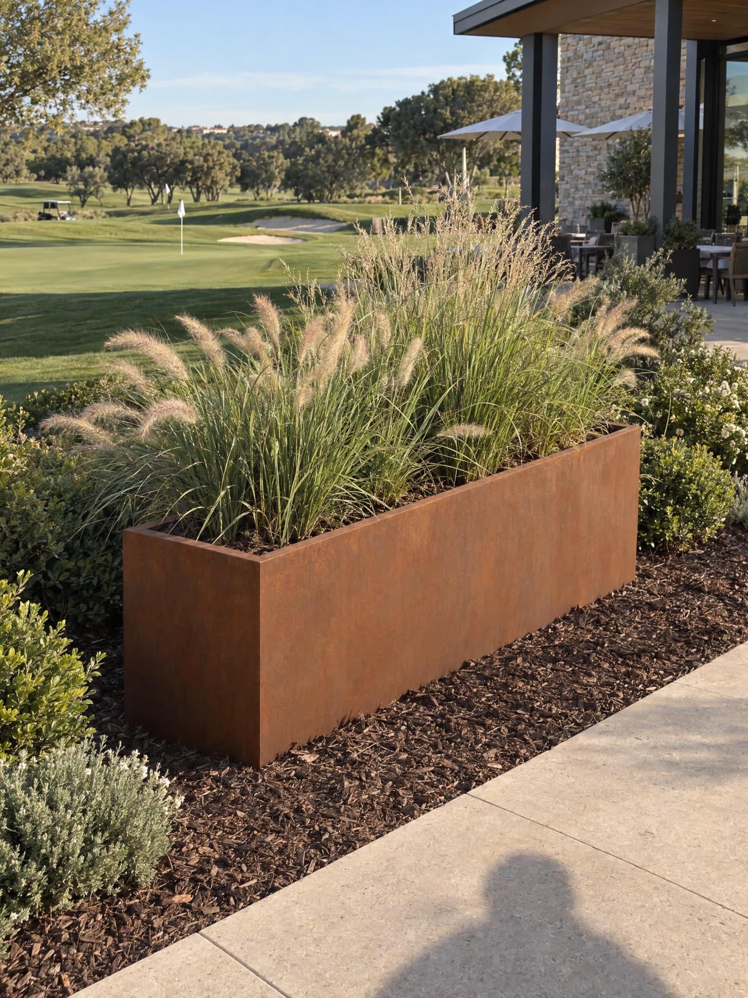 Gaia bottomless rectangular Corten steel planter planted with grasses along a golf course path