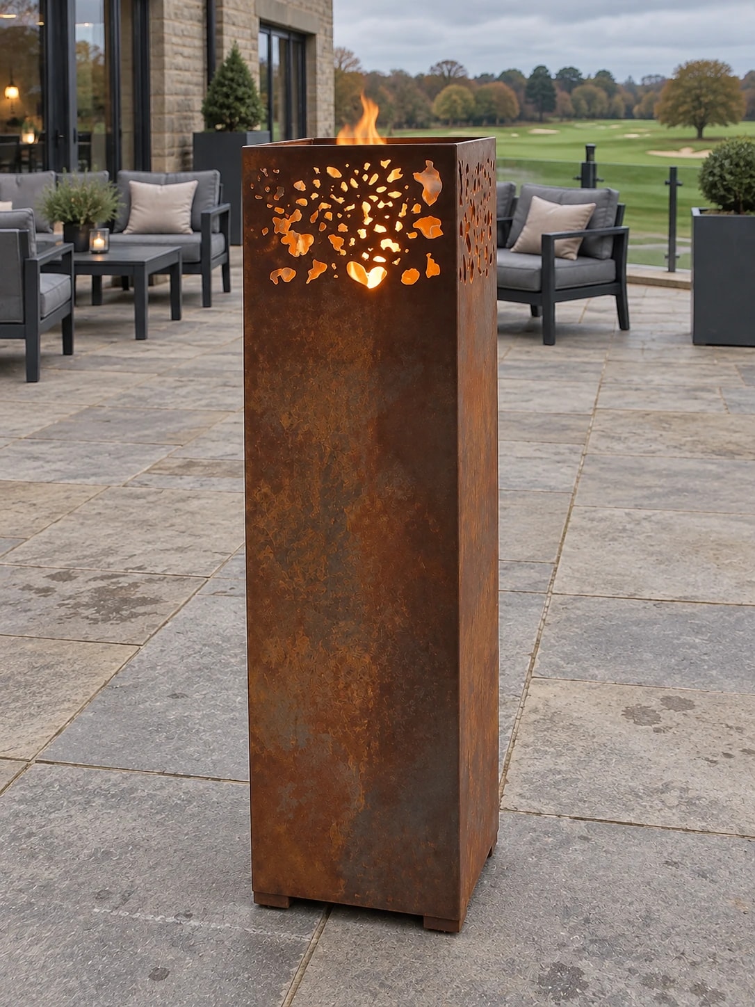 Lanterne Aurore en acier Corten allumée sur une terrasse face à un golf, salon d'extérieur gris derrière