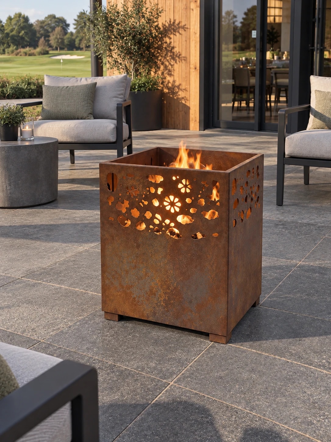 Lanterne Flora en acier Corten allumée sur une terrasse face à un golf, fauteuils d'extérieur