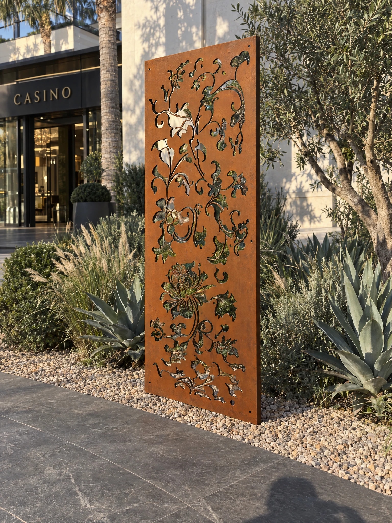 Panneau décoratif Auster en acier Corten dans un massif d'agaves et d'oliviers devant l'entrée d'un casino