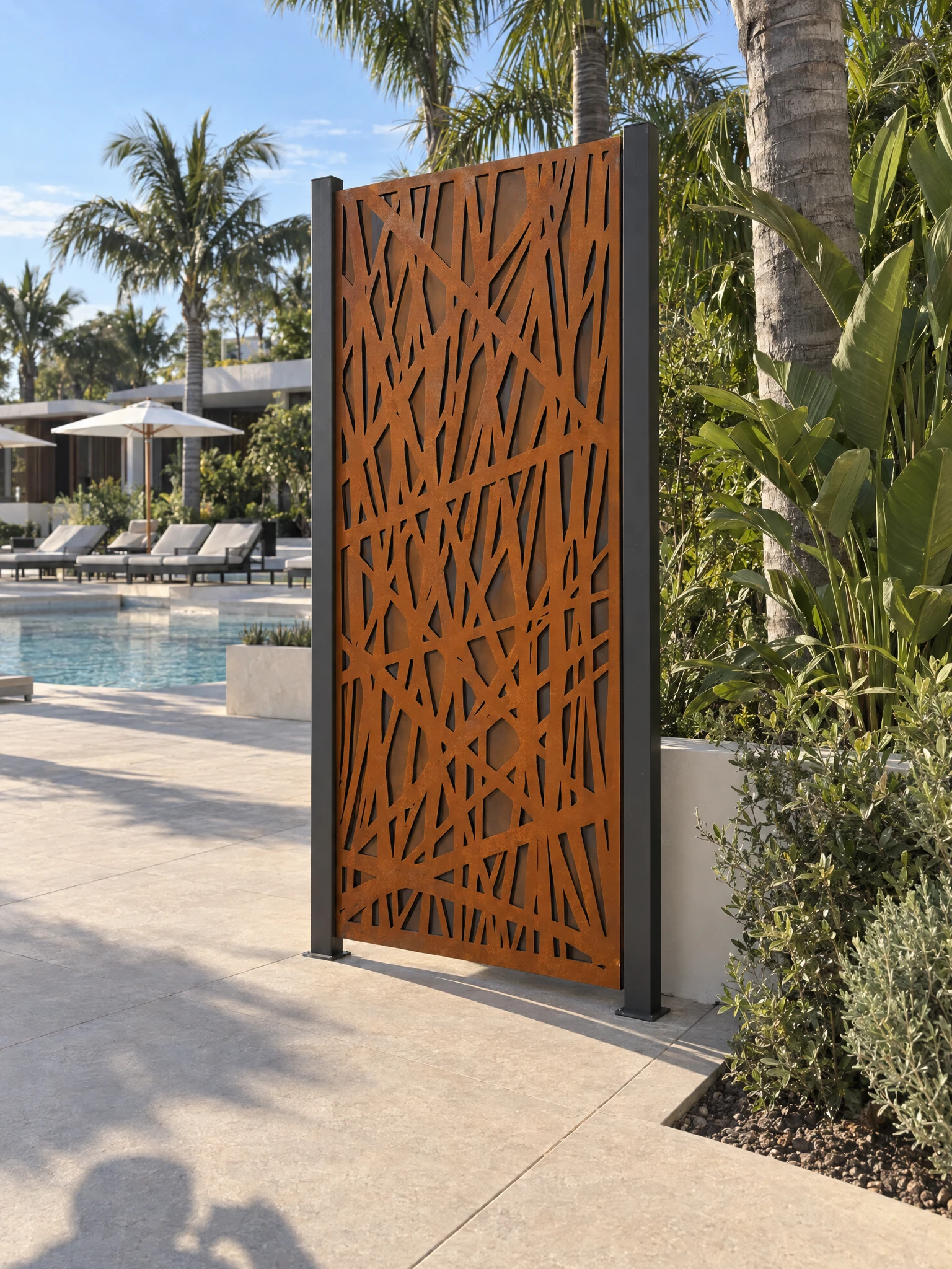 Panneau décoratif Harmattan en acier Corten entre deux poteaux au bord d'une piscine bordée de transats et de palmiers
