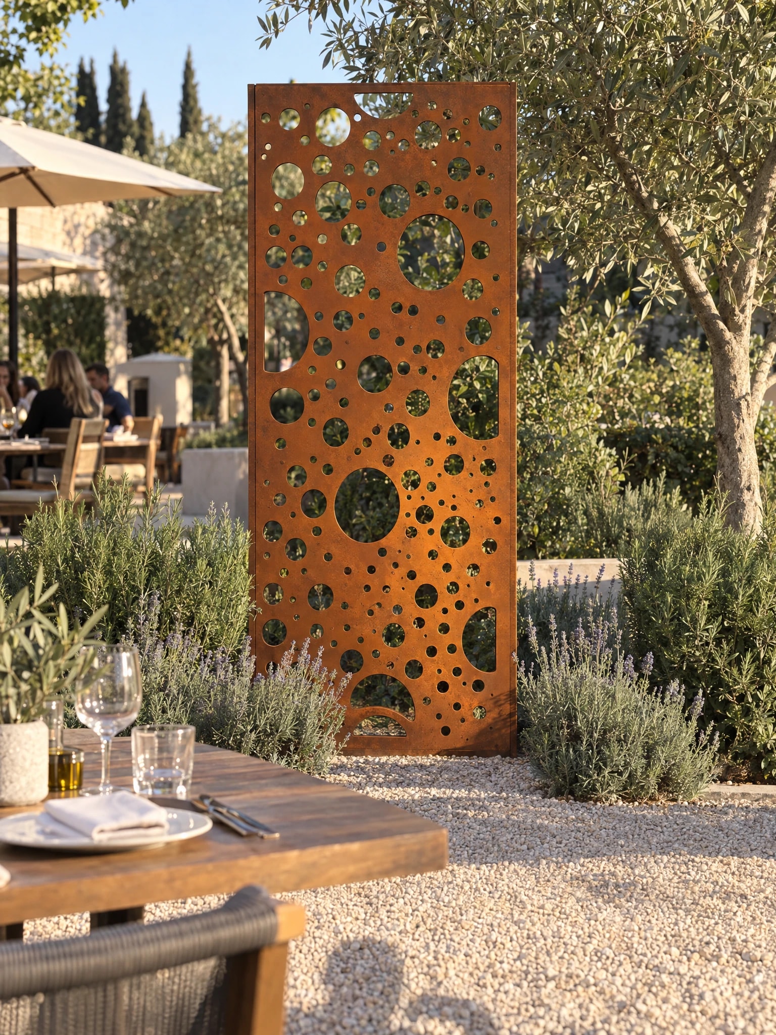 Panneau décoratif Notos en acier Corten dans un jardin de gravier près d'une table dressée sur une terrasse de restaurant