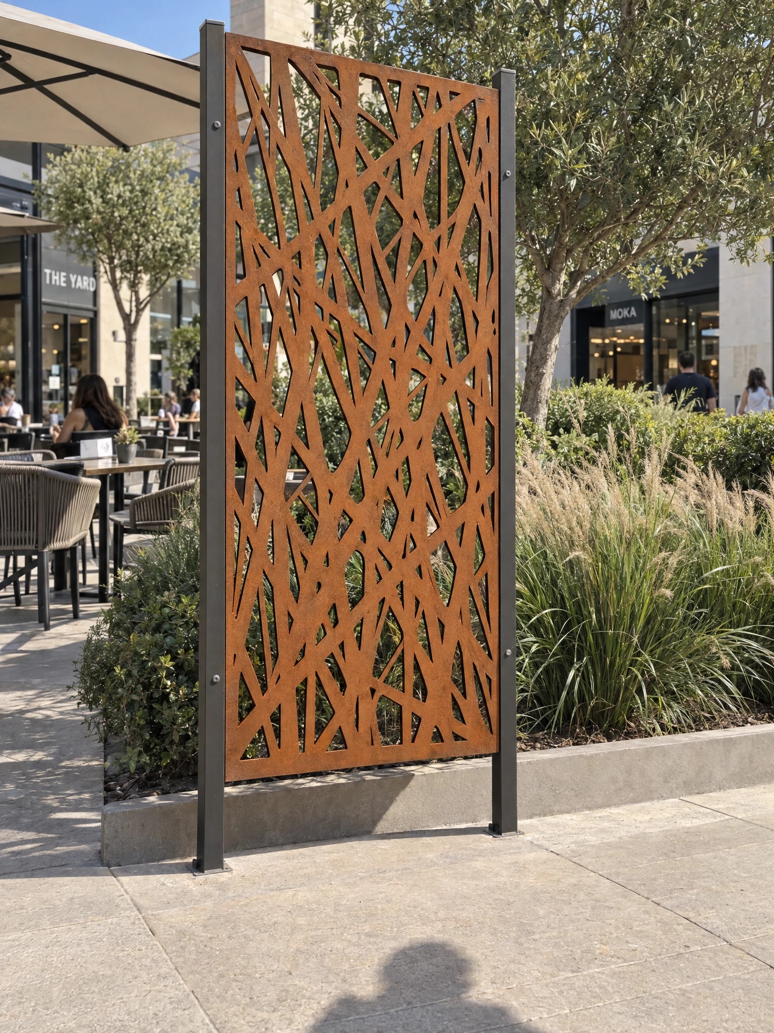 Panneau décoratif Euros en acier Corten entre deux poteaux dans un massif d'un centre commercial, terrasse de café au fond