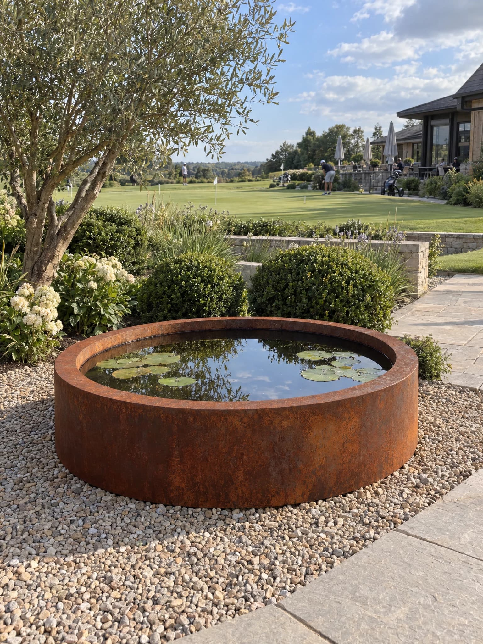 Bassin rond Ondine en acier Corten rempli d'eau et de nénuphars, sur un lit de gravier au bord d'un parcours de golf