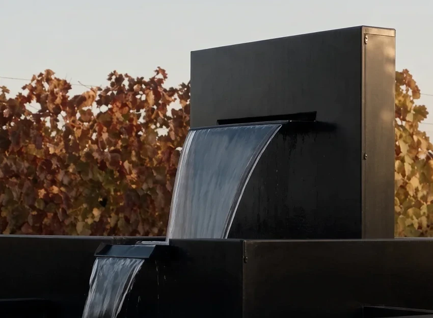 Fontaine cascade Nereida en aluminium noir devant un vignoble d'automne, une mariée debout à côté